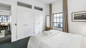 A hotel room with a bed, a wardrobe, a window with curtains, and a framed picture on the wall. - Gorgeous NY Style Loft in CBD | Netflix Wifi | (Auckland CBD)