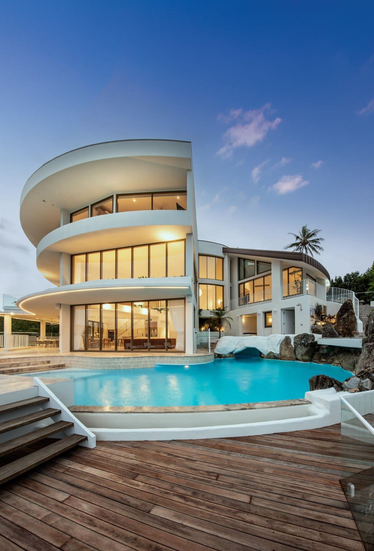 A modern multi-story house with a pool, featuring a curved design and large windows.