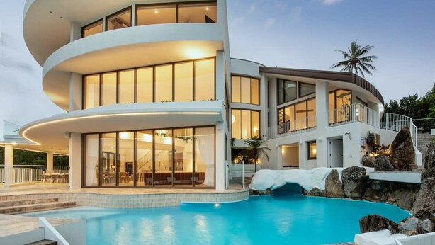 Une maison moderne à plusieurs étages, dotée d’une piscine, qui se distingue par son design aux lignes courbes et ses grandes fenêtres.