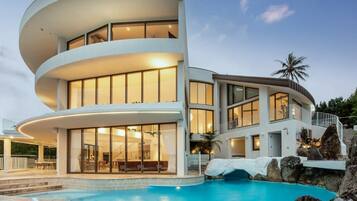 A modern multi-story house with a pool, featuring a curved design and a wooden deck.