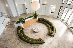 A spacious, modern interior with a curved green sofa arrangement, a central coffee table, and a staircase leading to upper floors. - Casa Rotunda (Whitsundays)