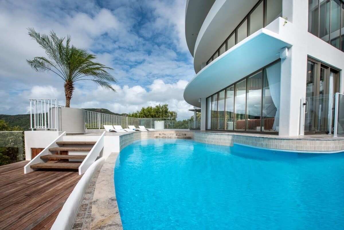 A modern pool area with a clear blue pool, wooden deck, and a palm tree.