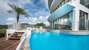 A modern pool area with a clear blue pool, wooden deck, and a palm tree.