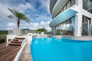 A modern pool area with a clear blue pool, wooden deck, and a palm tree. - Casa Rotunda (Whitsundays)