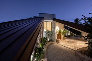 A modern building with a curved roof, a paved entrance area, and potted plants. - Casa Rotunda (Whitsundays)
