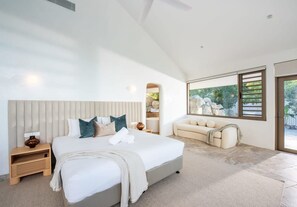 A modern bedroom with a large bed, a sofa, and a view of greenery. - Casa Rotunda (Whitsundays)