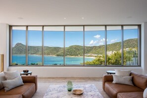 A room with a large panoramic window, a brown leather sofa, a marble coffee table, and a small side table. - Casa Rotunda (Whitsundays)