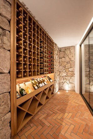 A wine cellar with wooden racks and a stone wall. - Casa Rotunda (Whitsundays)