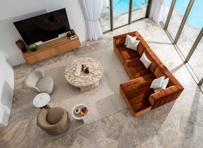 A modern living room with a large flat-screen TV, a brown sofa, a round coffee table, and a patterned rug. - Casa Rotunda (Whitsundays)