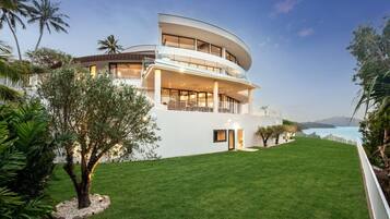 A modern two-story house with a curved facade, a well-maintained lawn, and a view of the sea.