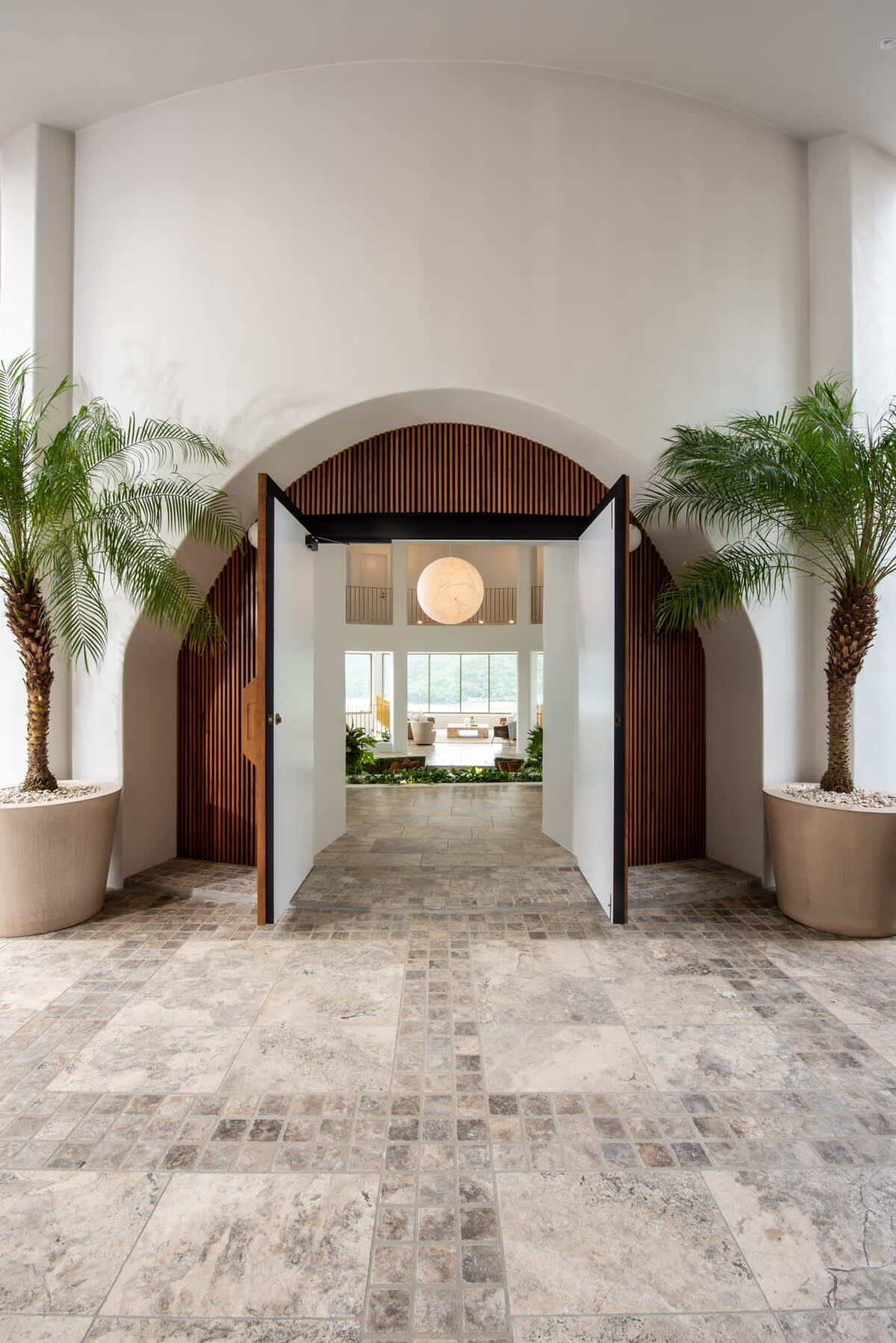 A spacious lobby with a high ceiling, a central open archway, and potted palm trees.