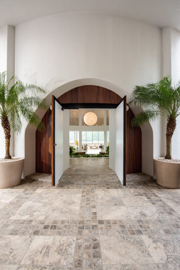 A spacious lobby with a high ceiling, a central open archway, and potted palm trees. - Casa Rotunda (Whitsundays)