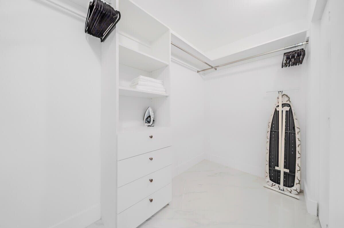 A white room with a wardrobe, a small ironing board, and a decorative door.