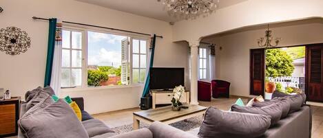 Un salon spacieux avec un grand canapé gris, un téléviseur à écran plat et un lustre.
