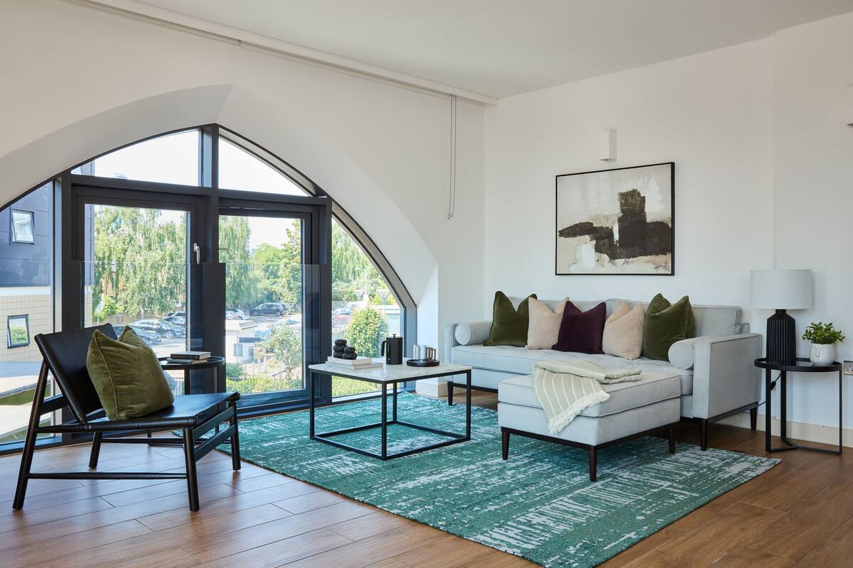 A modern living room with a large window, a white sofa, a black chair, and a coffee table.
