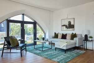 Una sala de estar moderna con un ventanal grande, un sofá blanco, un sillón negro y una mesa de centro.