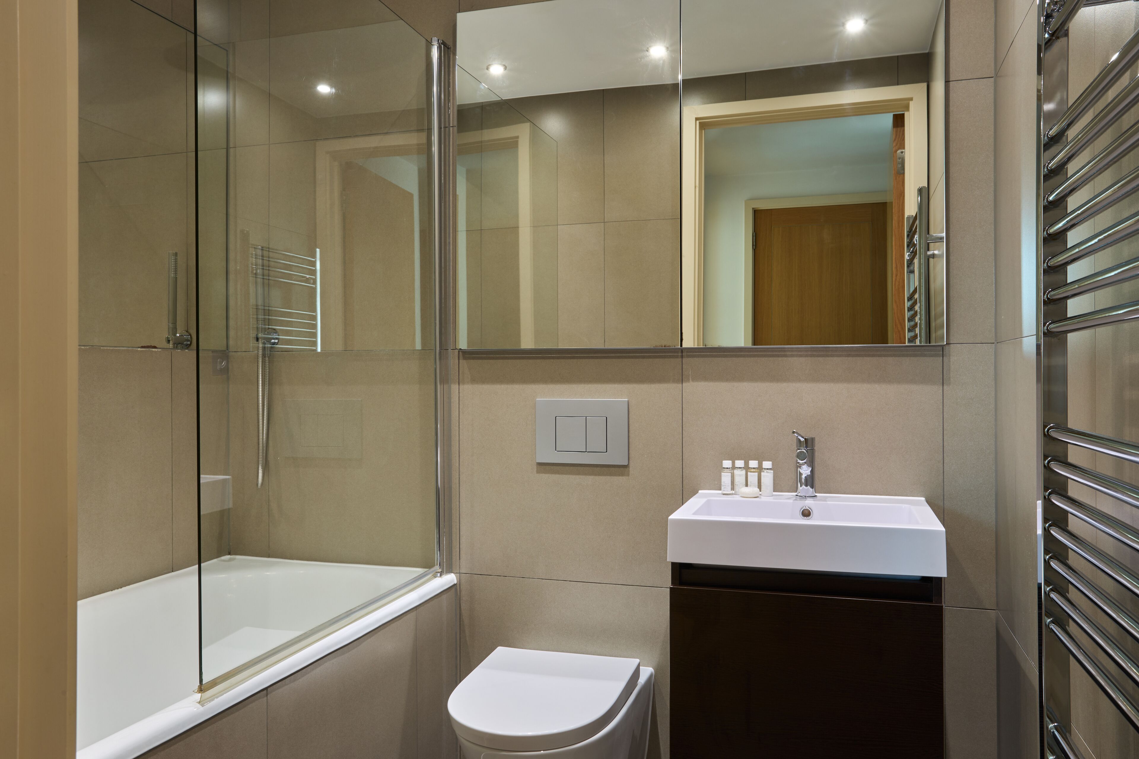 Een moderne badkamer met een glazen douchecabine, een witte wastafel en een toilet.