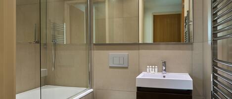Een moderne badkamer met een glazen douchecabine, een witte wastafel en een toilet.