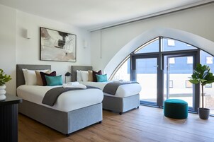 Un dormitorio moderno con dos camas, un ventanal grande y una planta en maceta.