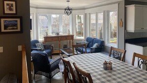 Un comedor con mantel a cuadros, sillas de mimbre y vistas al exterior a través de amplios ventanales.