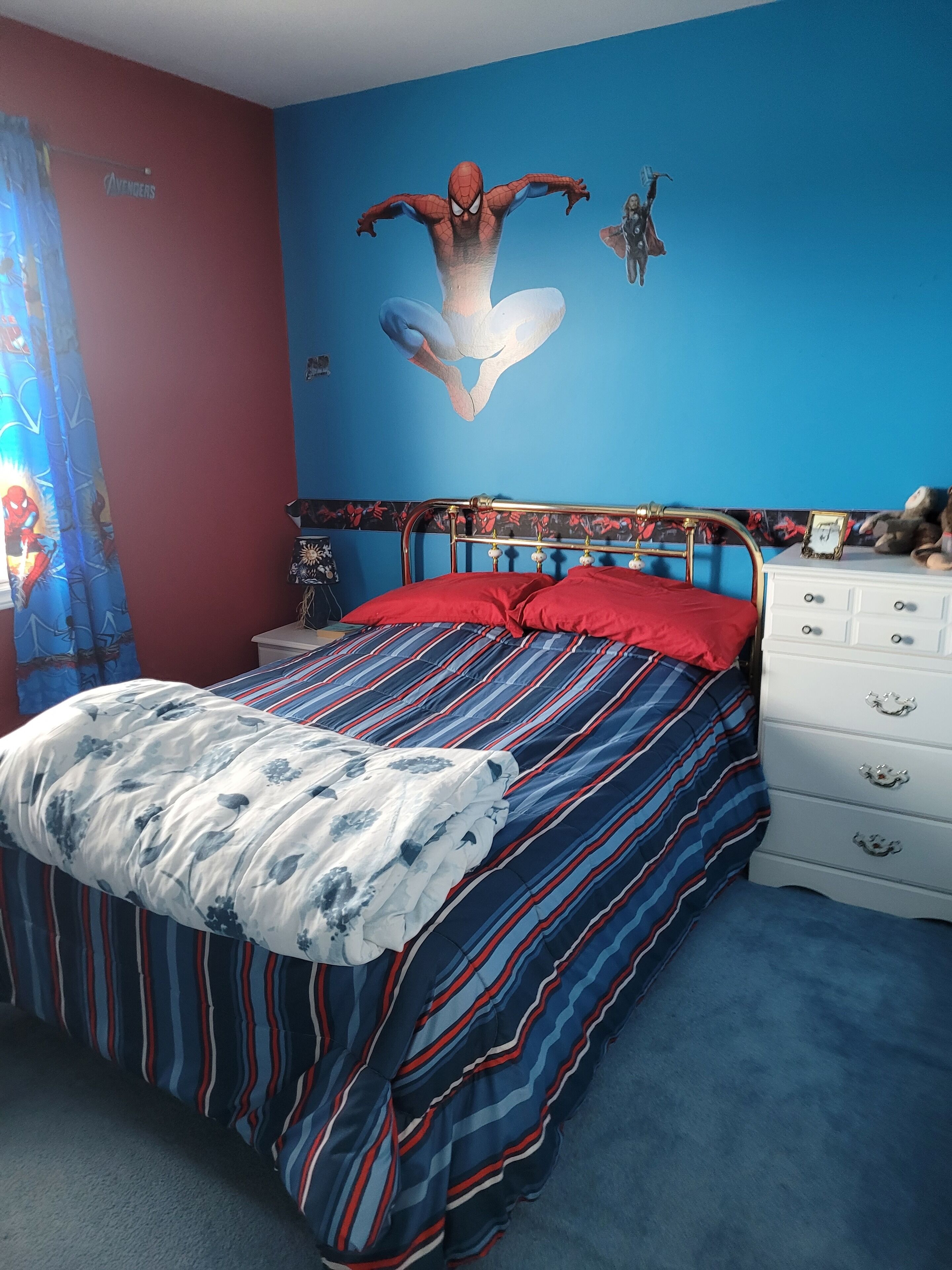 A bedroom with a bed, a dresser, and a wall mural.