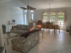 A living room with a sofa, a coffee table, a dining table with chairs, a ceiling fan, and a chandelier.
