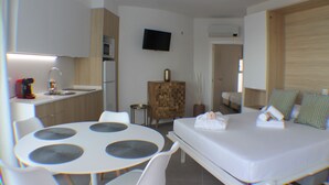 Moderni hotellihuone, jossa on sänky, yöpöytä ja pieni keittonurkkaus.
