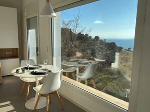 A dining area with a table and chairs, a potted plant, and a view of a coastal landscape through a large window. - Agi Castell Mar 1012 Apartamento for rent in Roses Girona. (Roses)