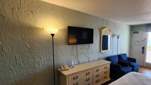Ein Hotelzimmer mit Bett, Wand-Fernseher, Schreibtisch mit Lampe, Stuhl und Blick ins Freie.