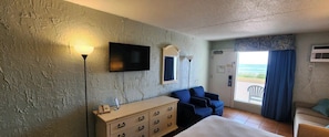 Ein Hotelzimmer mit Bett, Schminktisch, Fernseher, Stuhl und Blick auf den Ozean.