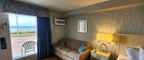 Ein Zimmer mit einer Couch, einem Nachttisch mit Lampe, einem gerahmten Bild an der Wand und einer Klimaanlage.
