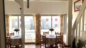 A dining area with two round tables, each with a vase of flowers, set against a large window with curtains. - CROMLEC'H - Duplex, Aperçu Mer - DT170 (Carnac)
