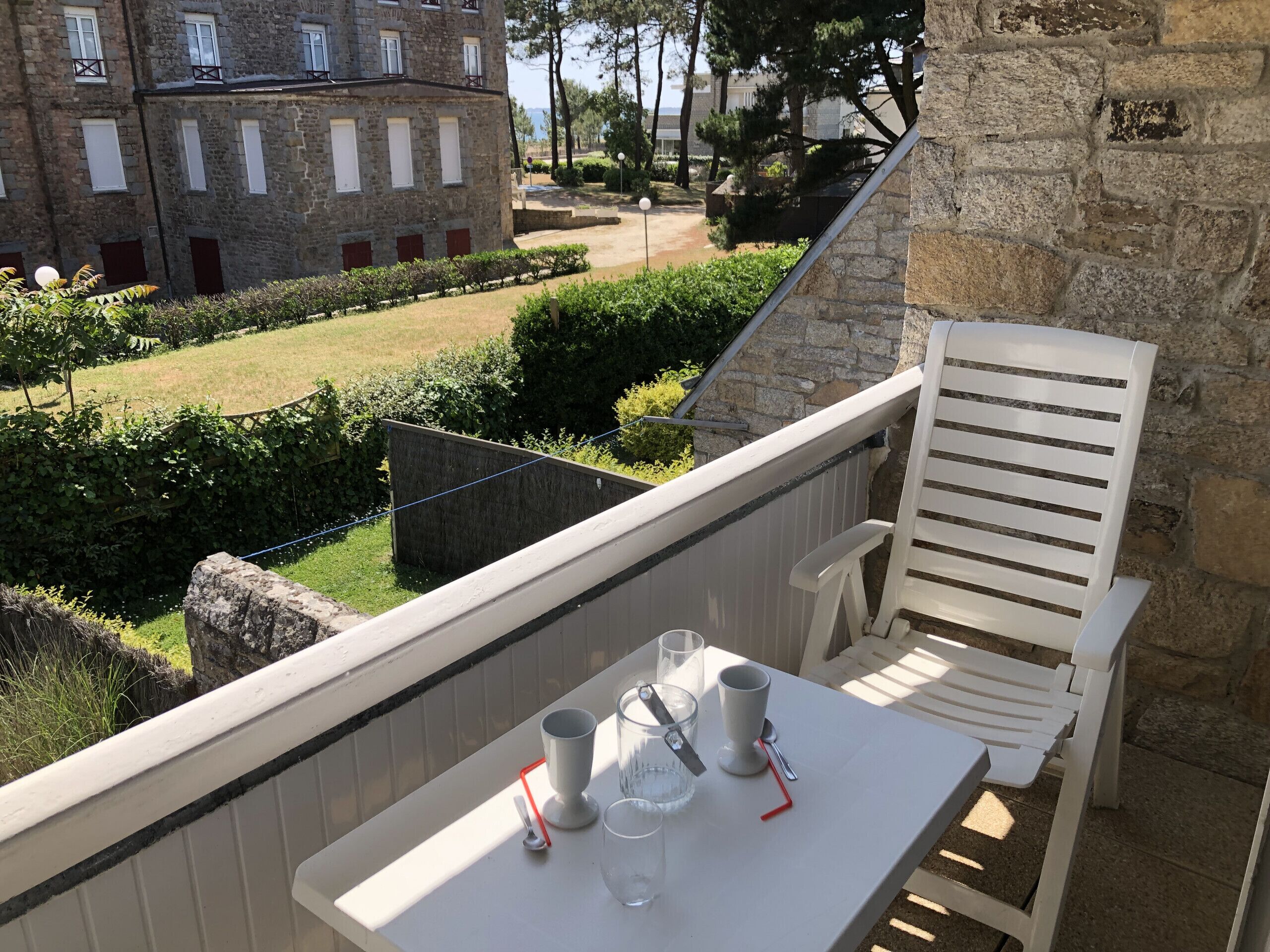 Un balcon avec une table, deux chaises et une vue sur un bâtiment en pierre et un jardin.