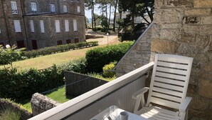 A balcony with a table, two chairs, and a view of a stone building and a garden. - CROMLEC'H - Duplex, Aperçu Mer - DT170 (Carnac)