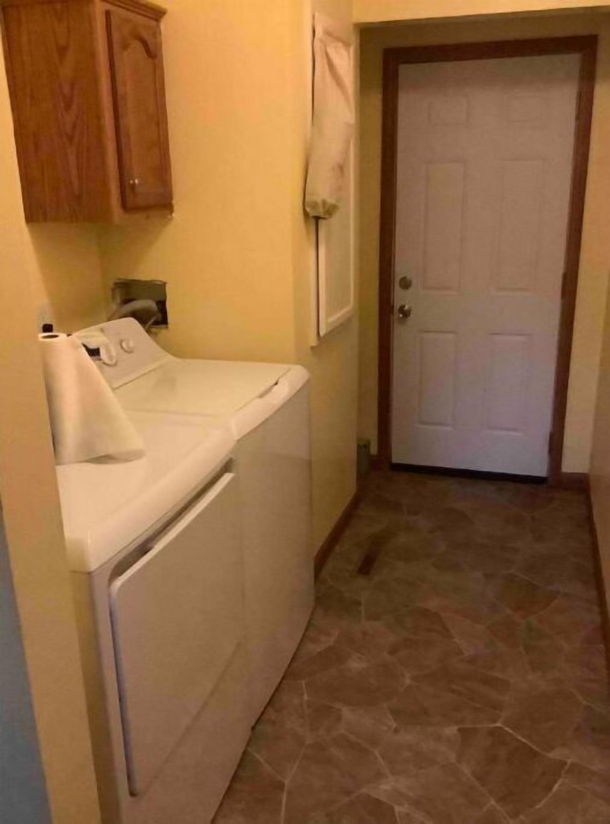 Un área de lavandería con lavadora, secadora y una puerta que da a otra habitación.