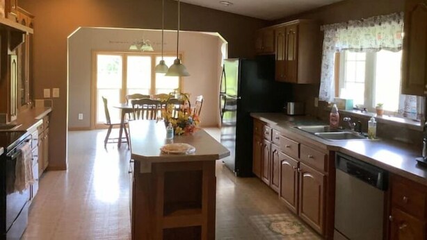 A spacious kitchen with wooden cabinets, a central island, pendant lighting, and a large window providing natural light.