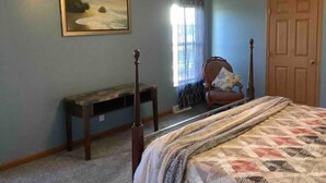 A bedroom with a bed, a chair, a wooden bench, a door, and a painting on the wall.