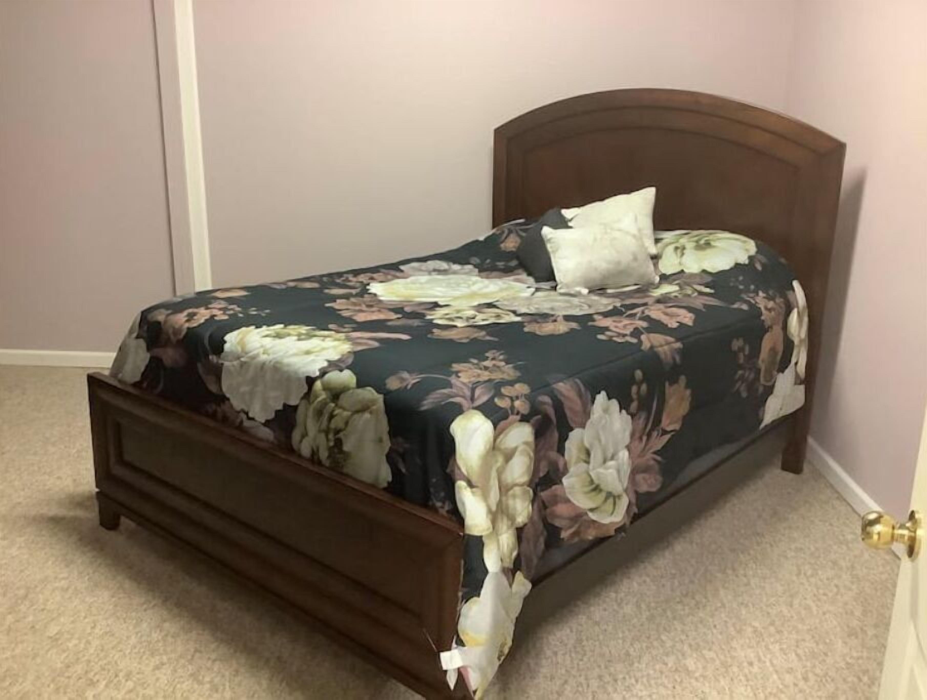 Un lit avec une couvre-lit à motifs floraux, une tête de lit en bois et un seul oreiller blanc.
