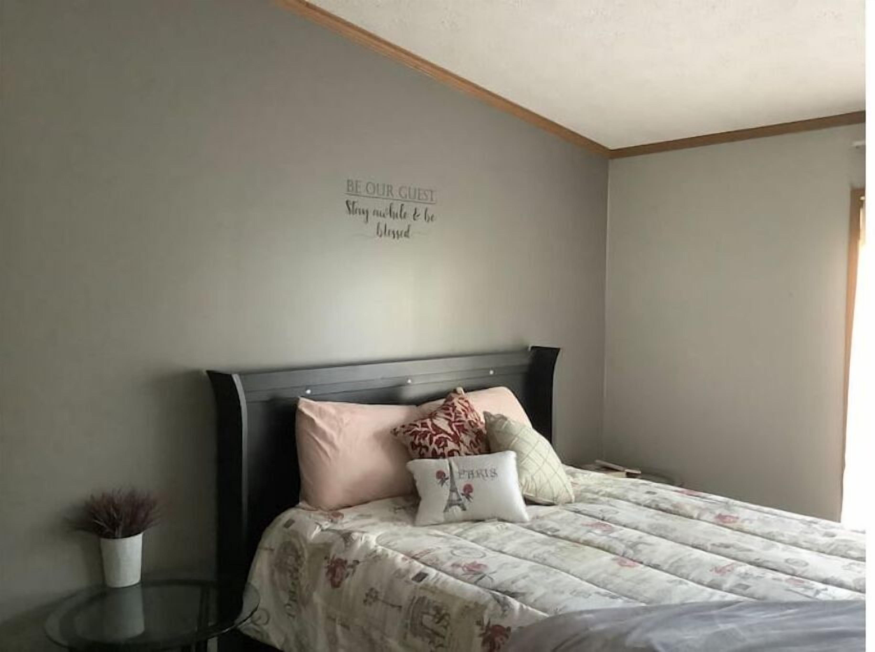 A bedroom with a bed, a bedside table, a wall with a motivational quote, and a small potted plant.