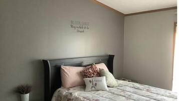 A bedroom with a bed, a bedside table, a wall with a motivational quote, and a small potted plant.