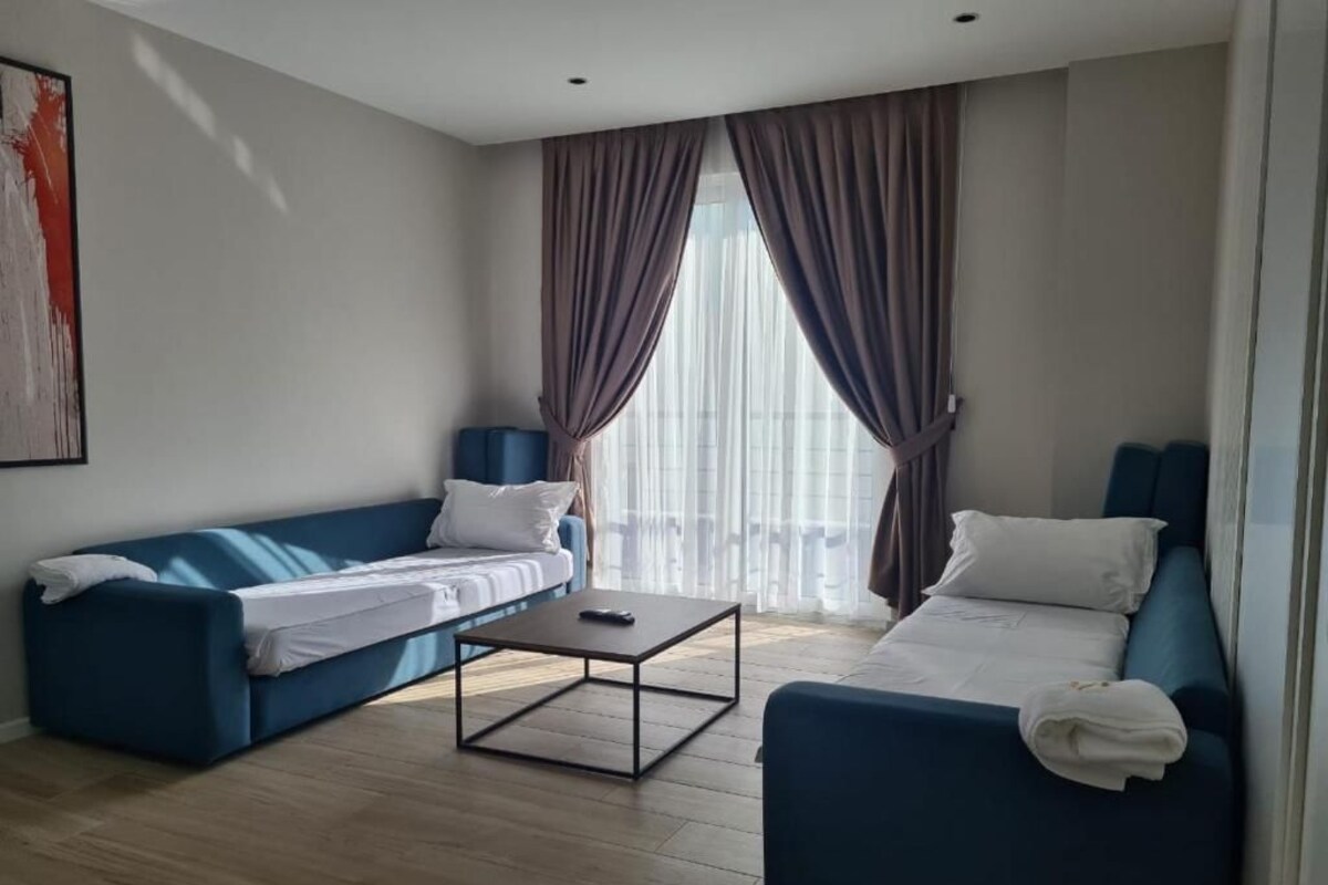 A modern hotel room with a blue sofa, a smaller sofa, a coffee table, and a bed with white bedding.