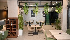 A modern cafe with wooden tables and chairs, a wine rack, and hanging plants. - Hotel Vino (Durrës)