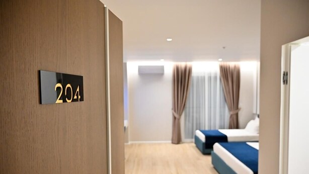 A hotel room with a wooden floor, two beds with blue bedding, a wall-mounted number sign '204', and a window with curtains. - Hotel Vino (Durrës)