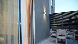 A modern outdoor patio with a glass door, a wall-mounted light, and a seating area with chairs. - Hotel Vino (Durrës)