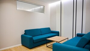 A modern living room with a blue sofa, a wooden coffee table, and a white wall with a vertical panel design. - Hotel Vino (Durrës)