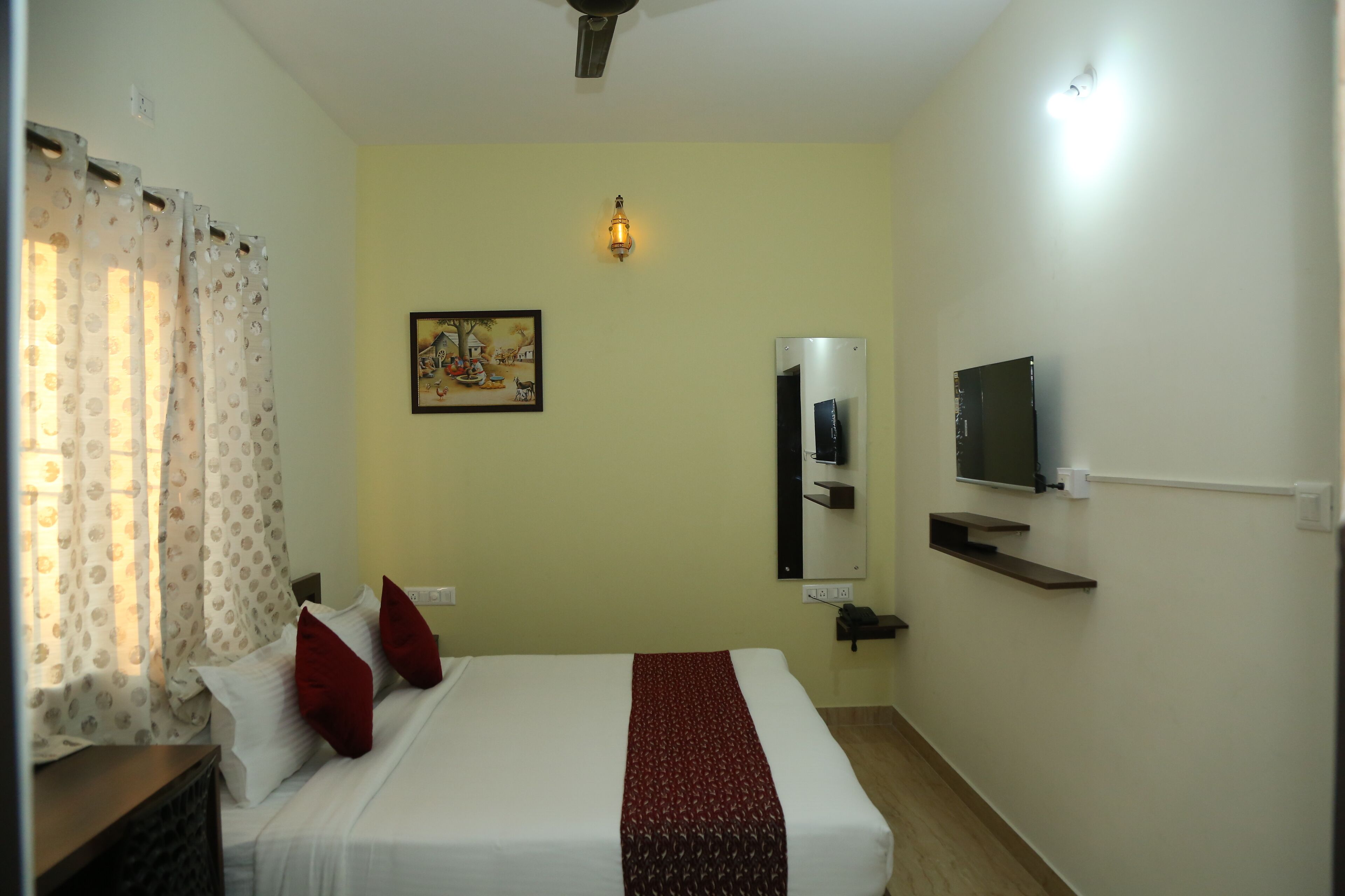 Una habitación de hotel con una cama, televisión, estante en la pared y un cuadro.