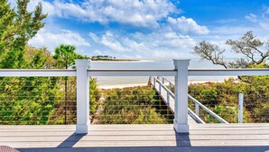 A wooden deck with a railing, overlooking a beach and ocean.