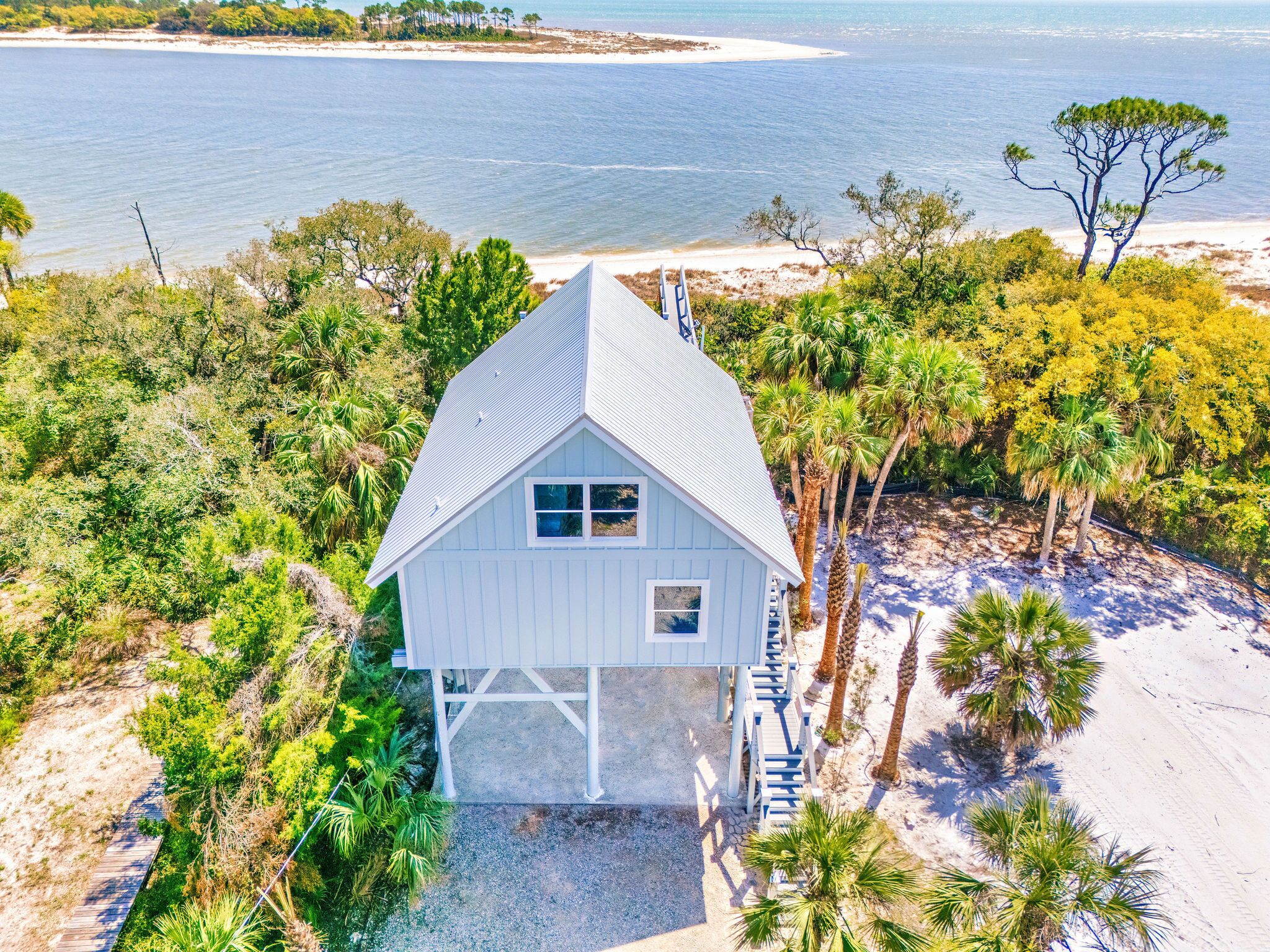 Une maison blanche avec un toit à pignon, entourée de palmiers et bordée par une plage.