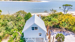 A white house with a gabled roof, surrounded by palm trees and a beach.
