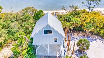 Une maison blanche avec un toit à pignon, entourée de palmiers et bordée par une plage.